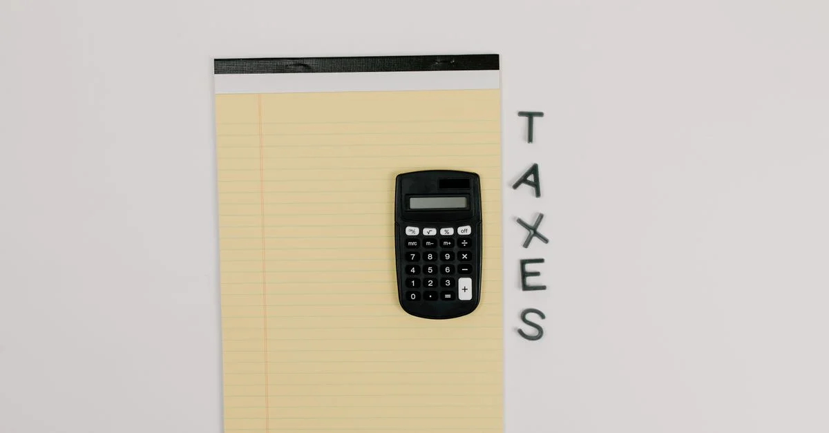 Vue de dessus d'une calculatrice sur un bloc-notes jaune avec le mot 'IMPÔTS' à côté.