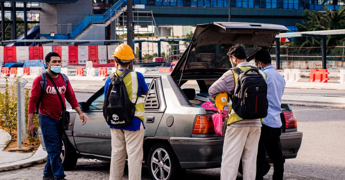 Des hommes portant des casques de sécurité et des masques chargent le coffre d'une voiture à côté d'un chantier pendant la journée.