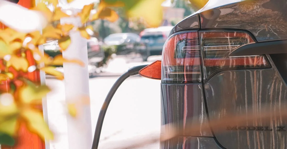 Gros plan d'une voiture électrique connectée à une station de charge en plein air sous le soleil.