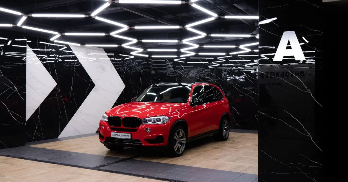 SUV rouge présenté dans un showroom élégant avec un éclairage géométrique et des murs en marbre.