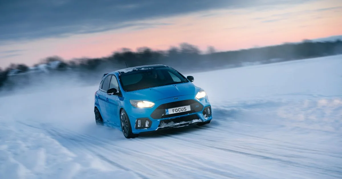 Prise de vue dynamique d'une voiture de sport bleue dérapant sur une route rurale enneigée au coucher du soleil.