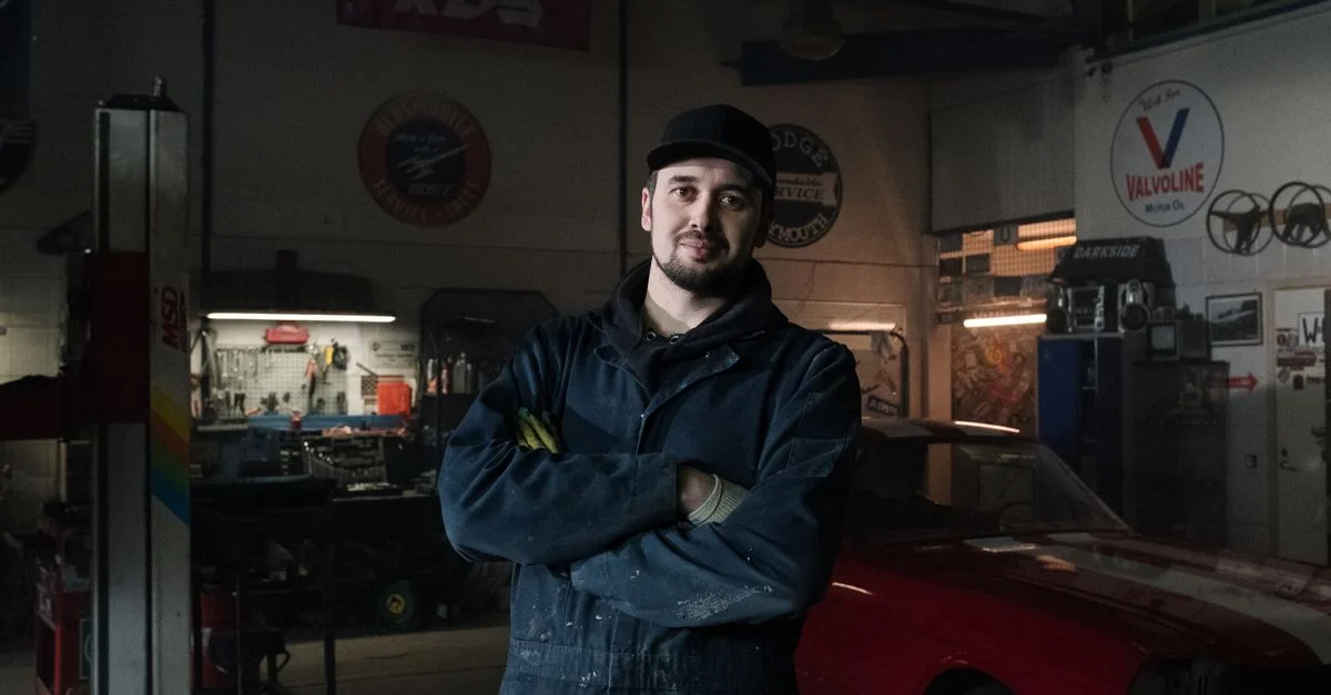Mécanicien expérimenté dans un garage vintage se tenant confiantly à côté d'une voiture classique.