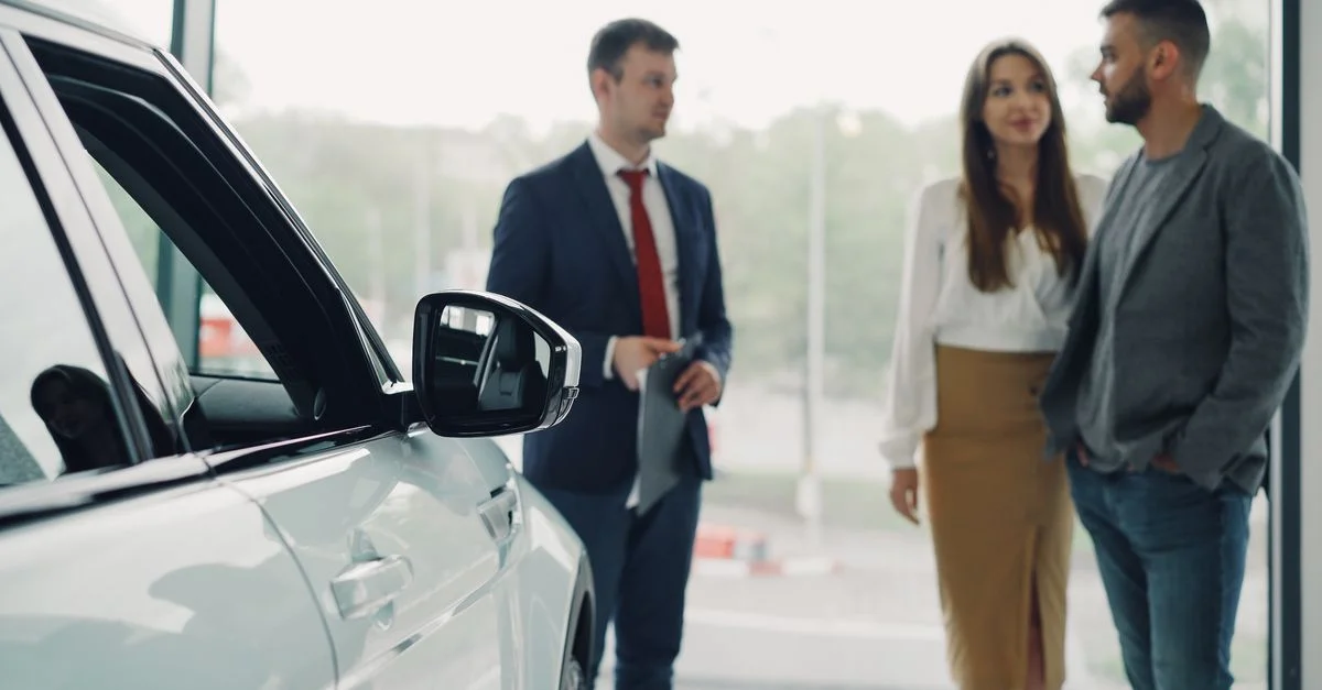 Un vendeur conseille un couple dans une concession automobile moderne.