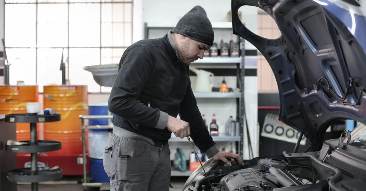 Mécanicien vérifiant le moteur d'une voiture dans un garage, assurant un entretien et une réparation de qualité.