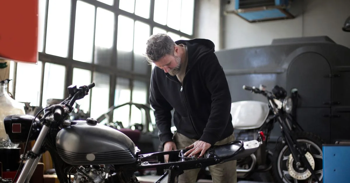 Un mécanicien barbu concentré sur la réparation d'une motocyclette dans un atelier.