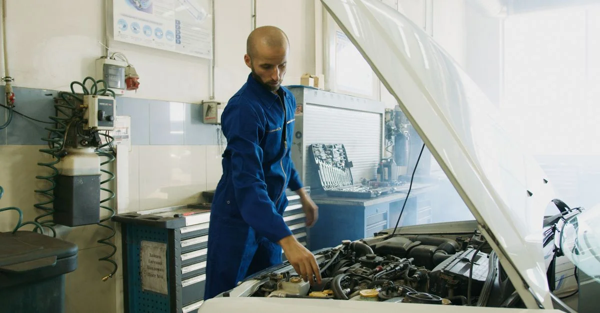 Mécanicien en uniforme bleu inspectant un moteur de voiture dans un atelier.