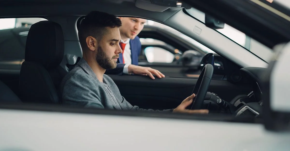 Un homme examine l'intérieur d'une voiture avec un vendeur dans une concession, en mettant en évidence les caractéristiques du véhicule.