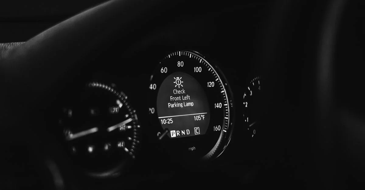 Gros plan sur un tableau de bord de voiture en noir et blanc, mettant en évidence le compteur de vitesse et les voyants d'avertissement.
