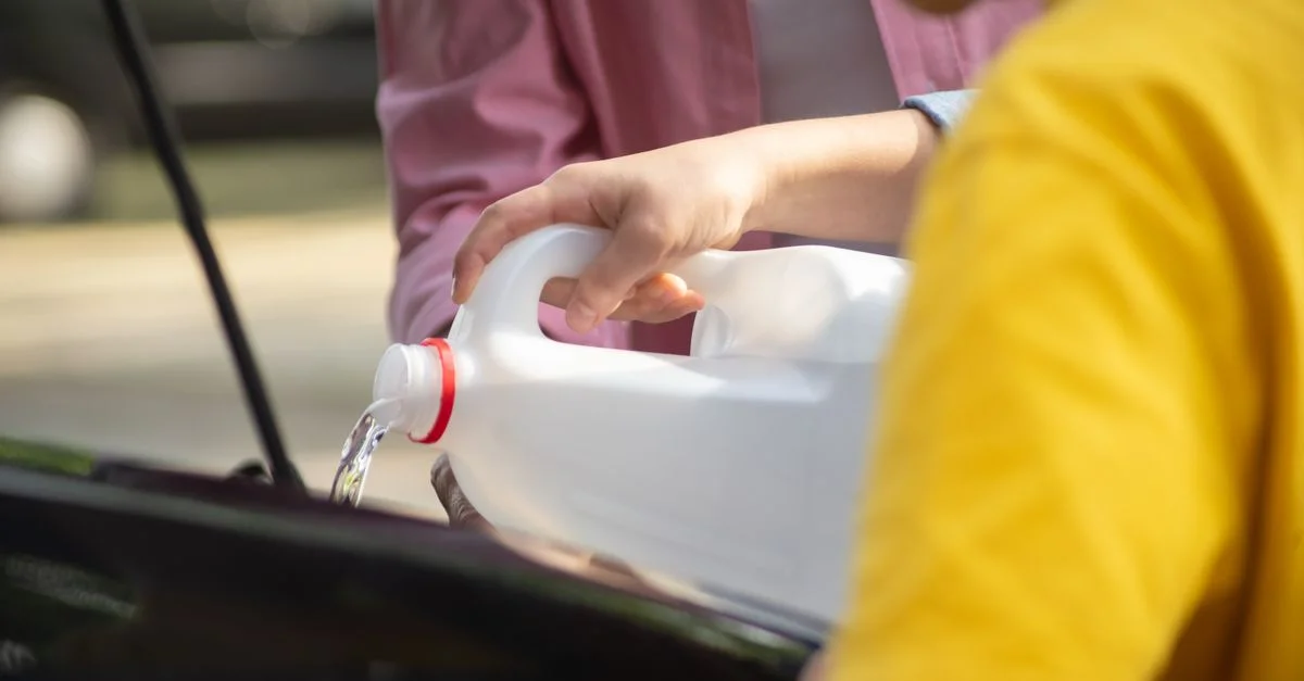 Gros plan sur des mains versant de l'eau dans un moteur de voiture, axé sur l'entretien automobile.