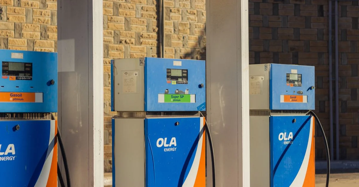 Trois pompes à essence OLA Energy bleues à une station extérieure par une journée ensoleillée.