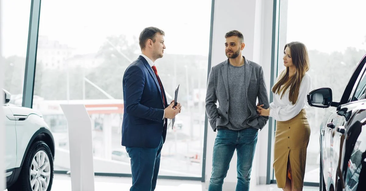 Un professionnel du commerce conseille un couple dans une concession automobile moderne.