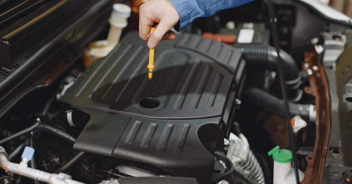 Gros plan d'une personne vérifiant l'huile du moteur à l'aide d'une jauge dans le compartiment moteur d'une voiture.