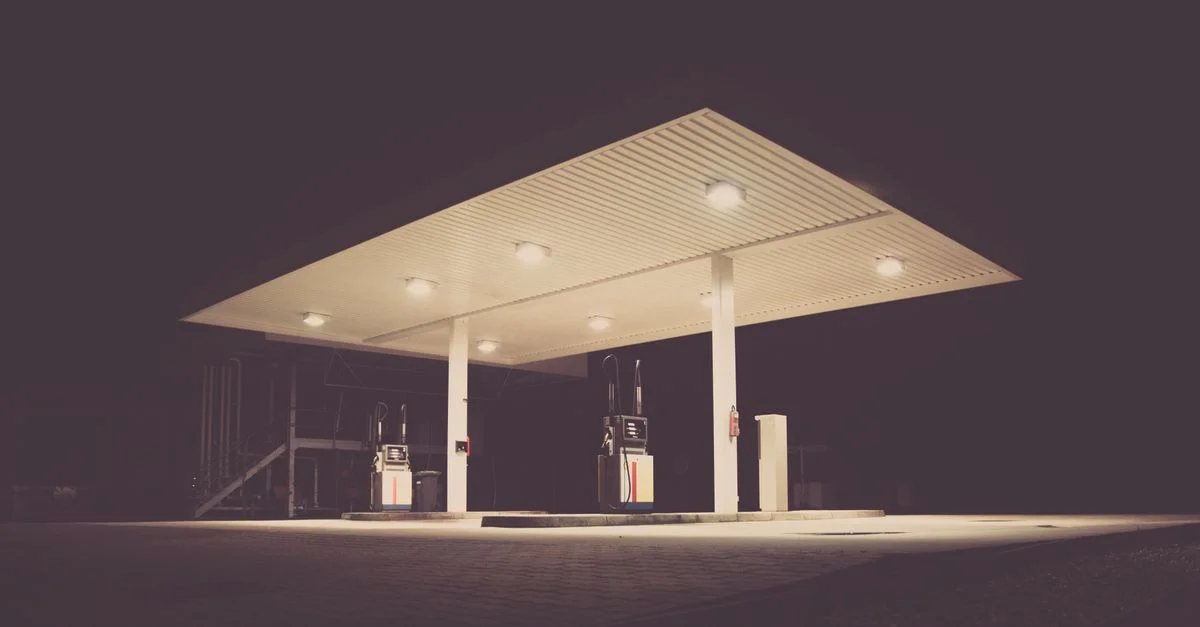 Une station-service faiblement éclairée la nuit, offrant une atmosphère inquiétante et calme avec un environnement sombre.