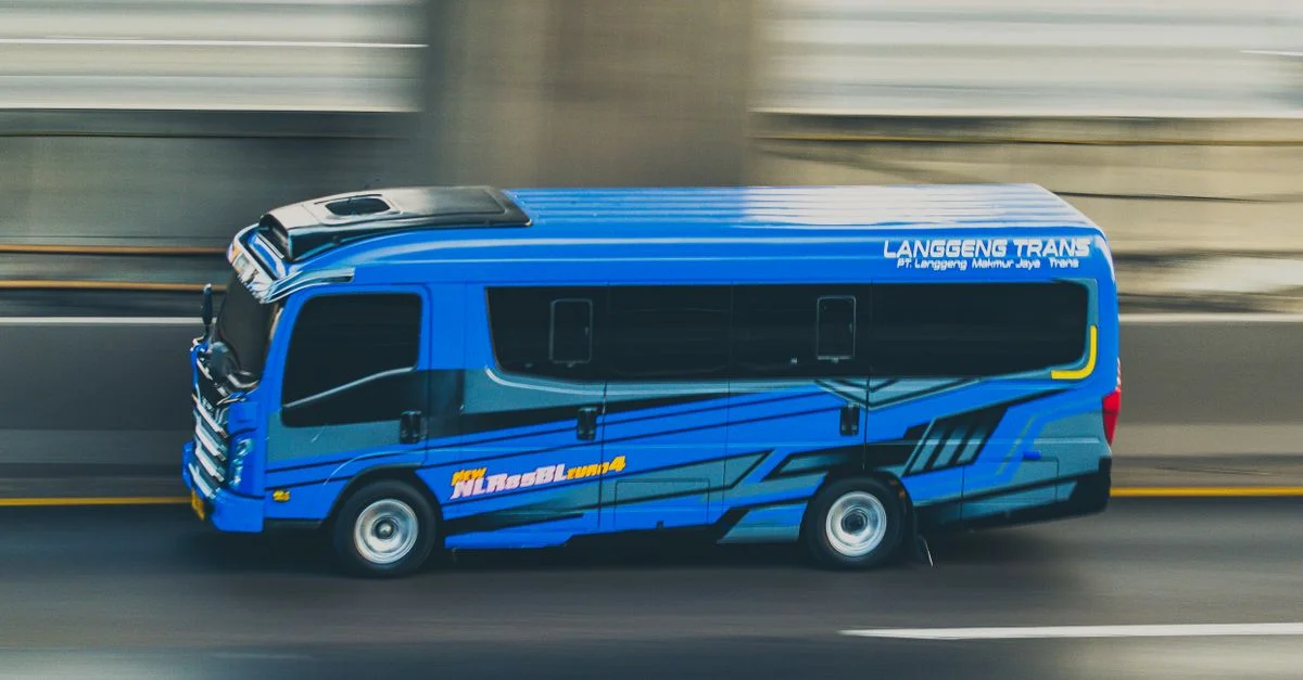 Un minibus bleu en mouvement, filmé par panoramique sur une autoroute.