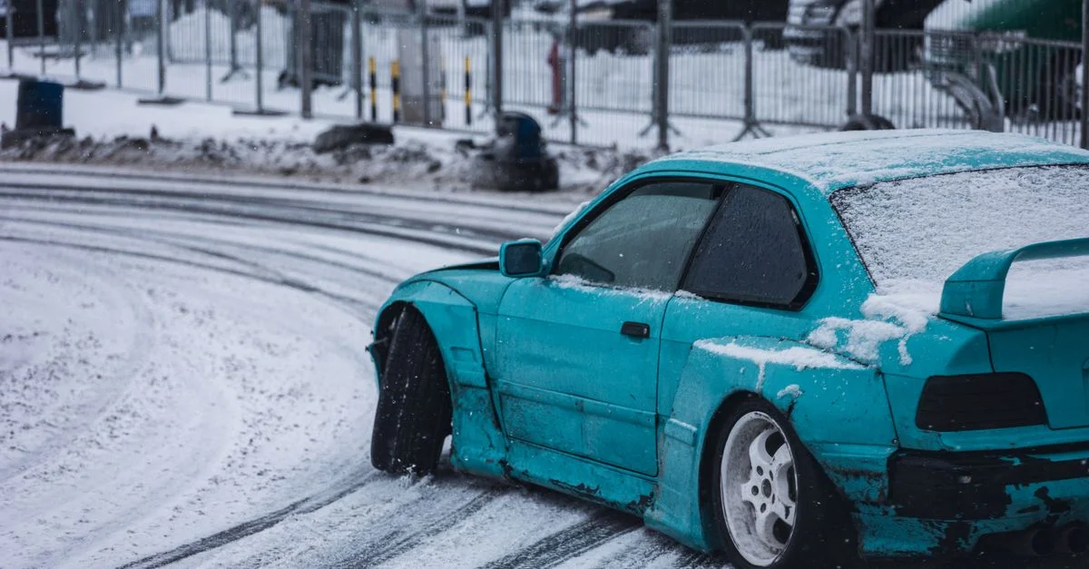 Voiture bleue effectuant un drift avec maîtrise sur une piste de course enneigée, mettant en avant l'action du sport automobile et les compétences de conduite hivernale.