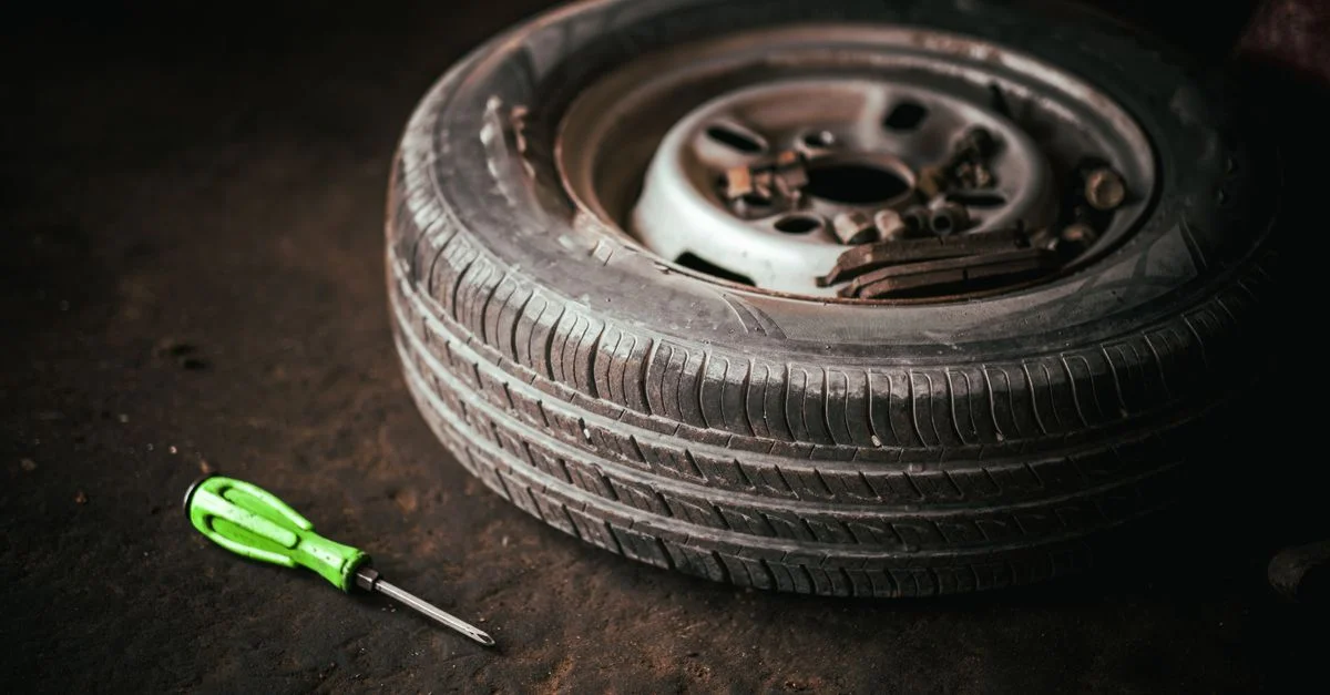 Un pneu de voiture et un tournevis vert posés sur le sol du garage, représentant la réparation automobile.