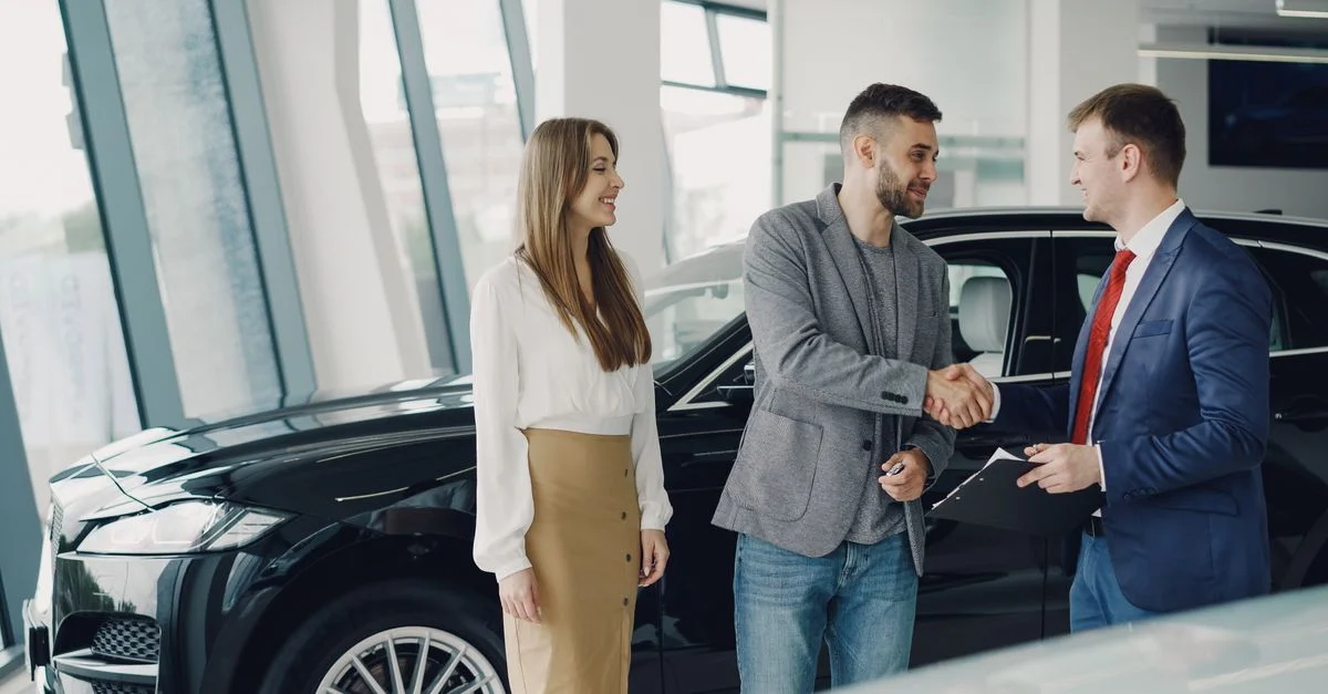 Clients serrant la main du concessionnaire dans le showroom, scellant l'accord d'achat d'une voiture.