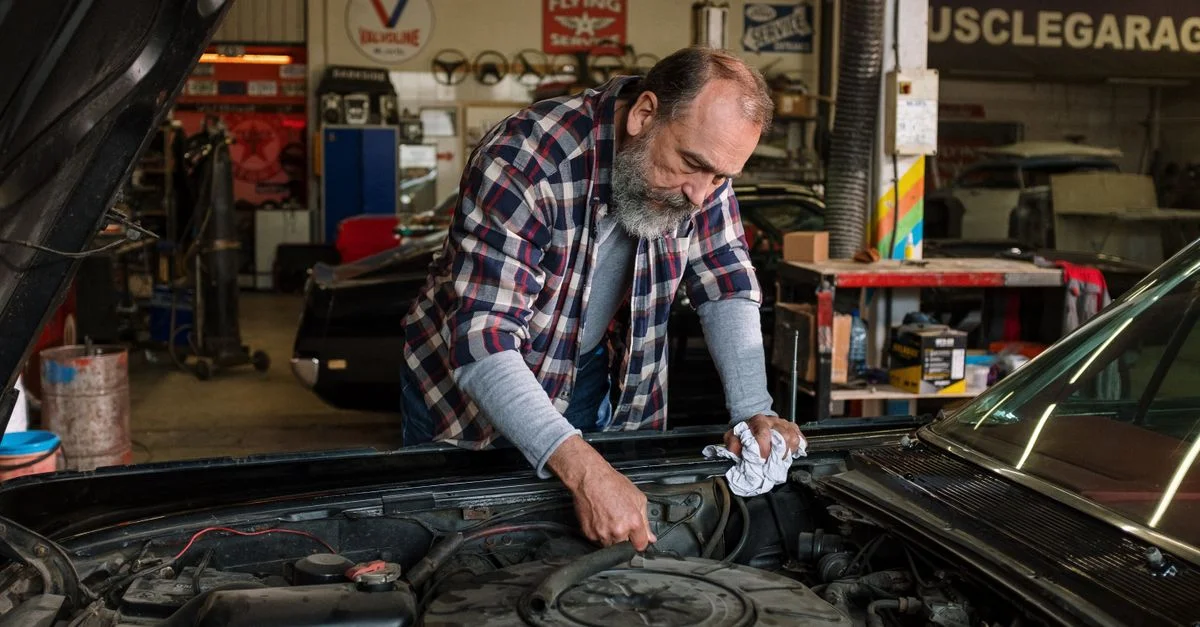 Mécanicien barbu travaillant sur la réparation du moteur dans un garage de réparation automobile avec un accent sur le service auto pratique.